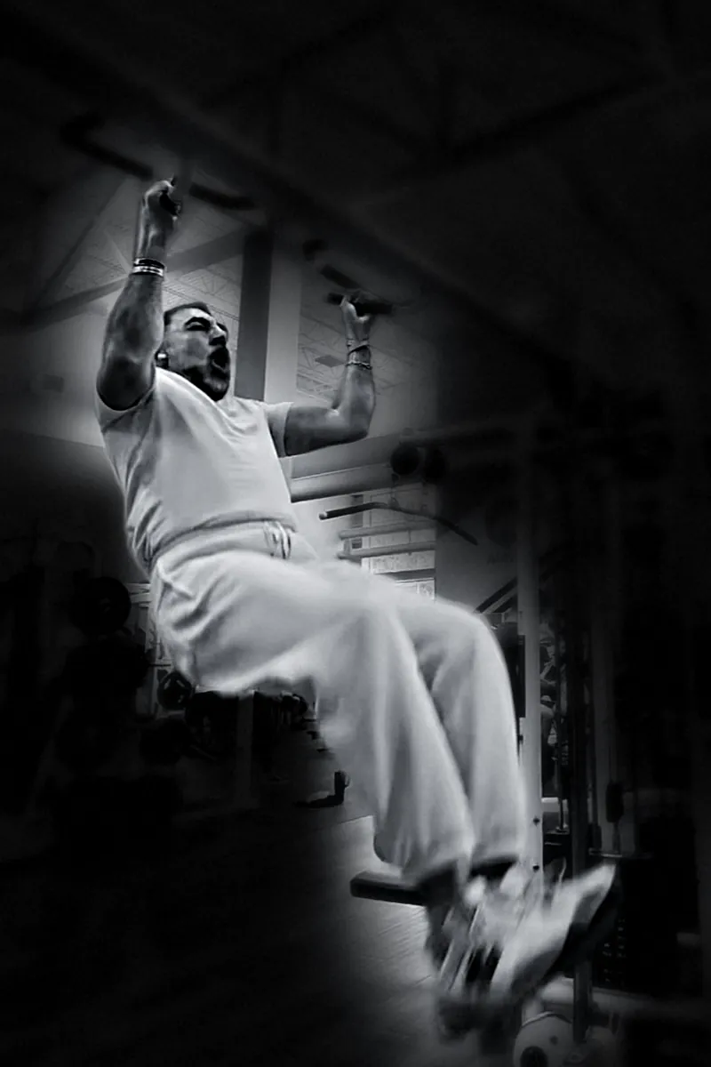 Houman Farzian in a hanging knee raise, shouting through the rep, black and white