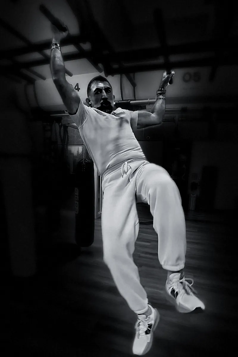Houman Farzian hanging from a pull-up bar, knees raised, black and white