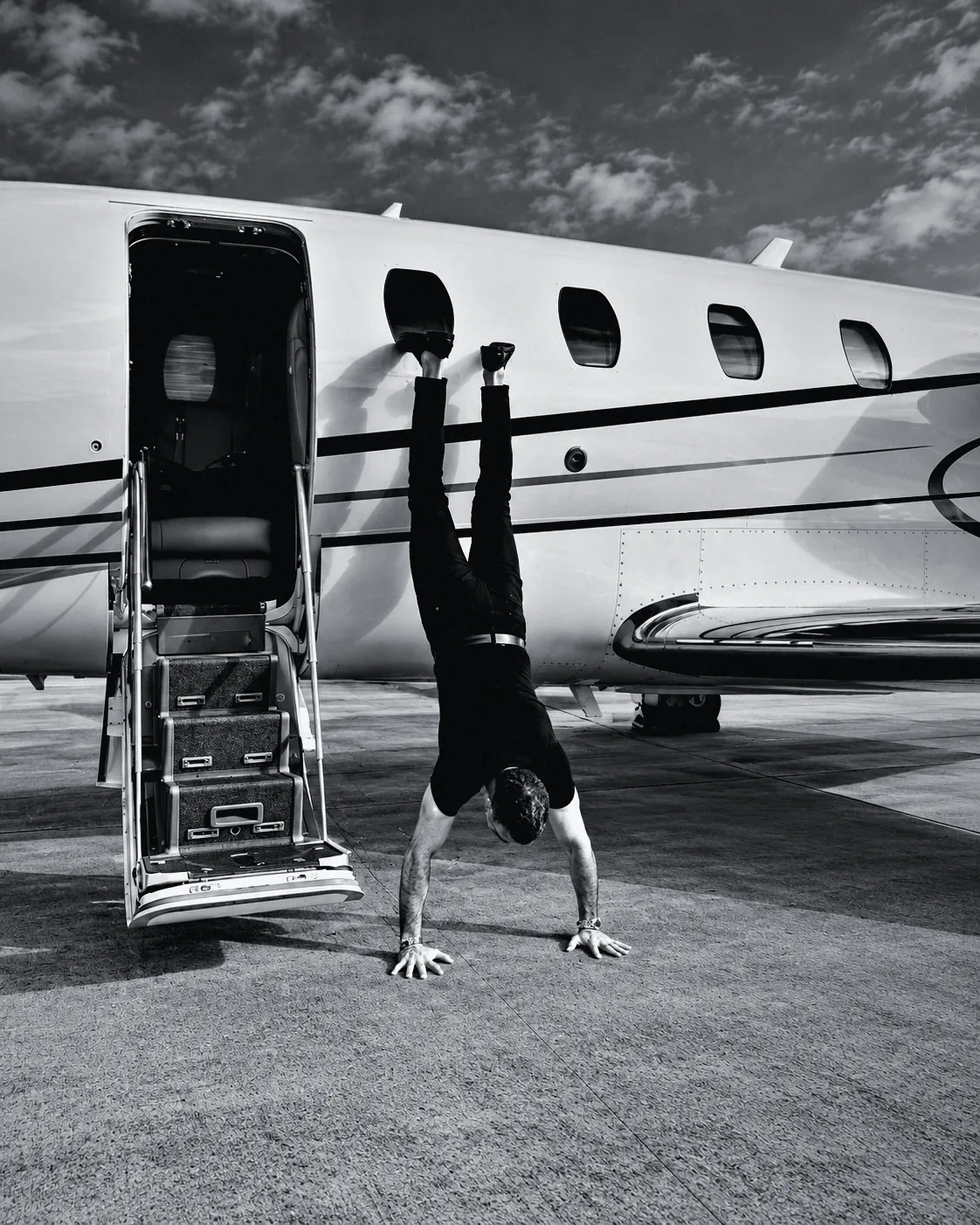 Houman Farzian in a handstand at the door of a private jet, black and white